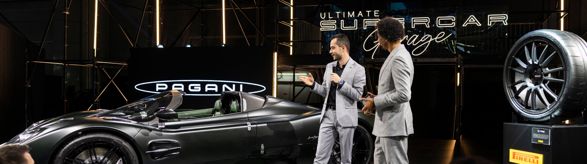 Photo noir et blanc d'une femme en tailleur avancant dans un hall d'exposition avec une supercar flou en fond