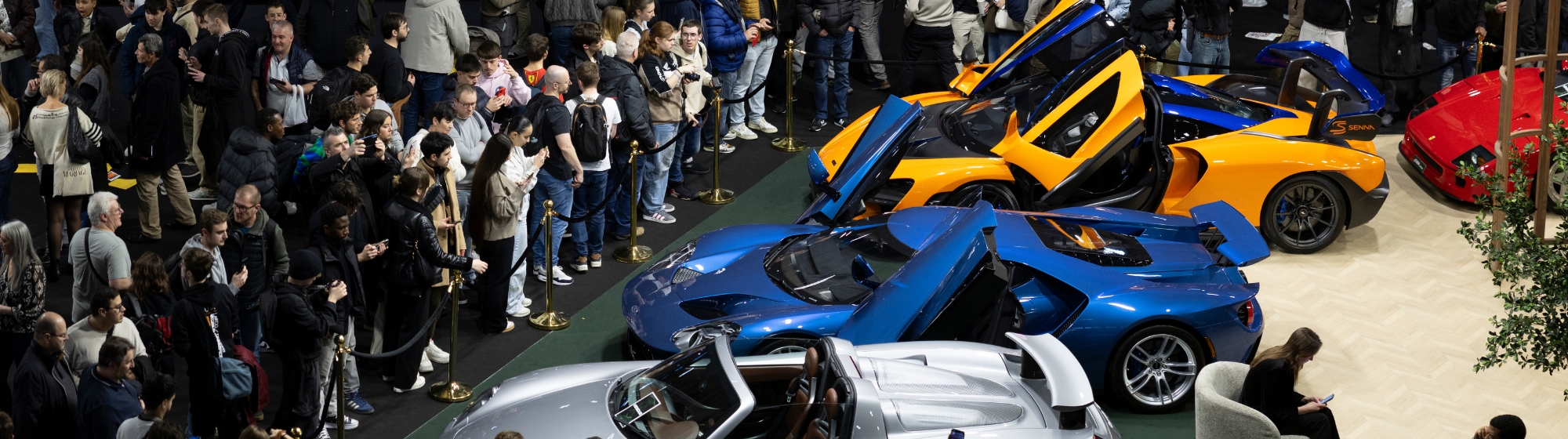Black and white view of a luxury hotel lobby with a visitor pulling a suitcase, and a high-end car visible in the background.