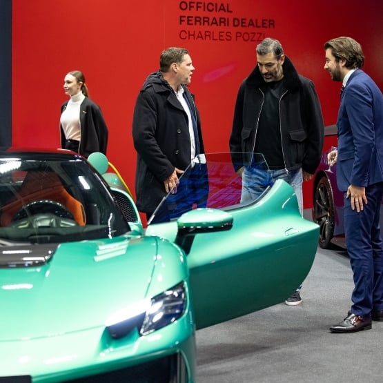 view of a VIP lounge at a luxury car show, with elegant guests engaging in discussion around exceptional vehicles, in a refined and exclusive atmosphere.