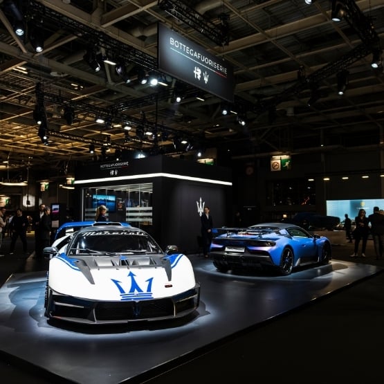 Photo d’une supercar mise en scène dans un espace d’exposition luxueux, avec éclairage dramatique, structure architecturale et ambiance élégante, suggérant une prise de parole sur scène.