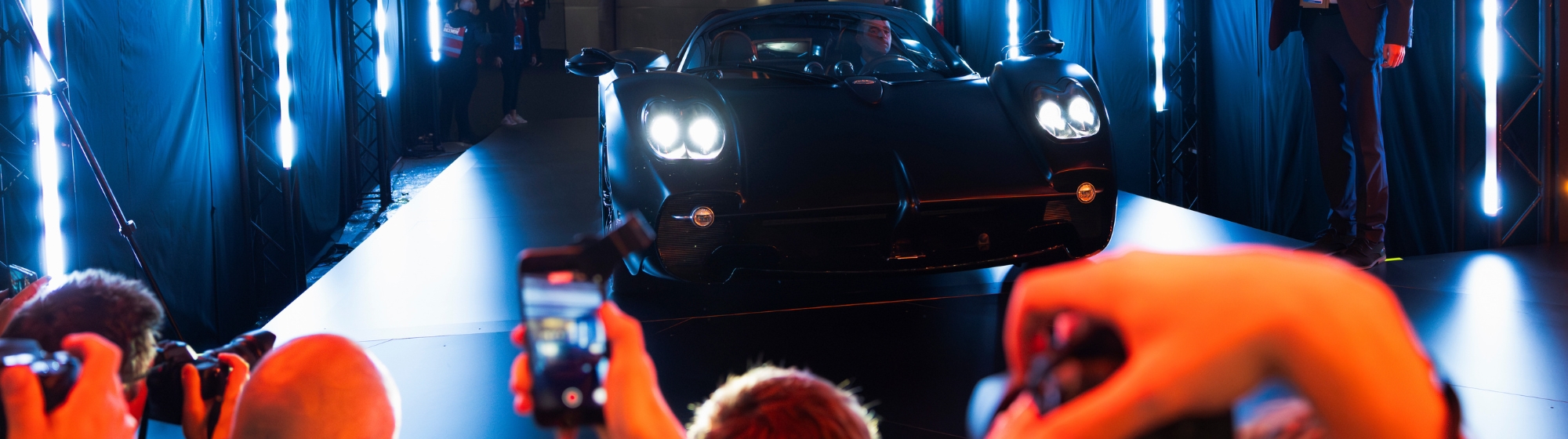 Black and white photograph of an influencer in a garage lit by neon lights, taking a selfie in front of a supercar.
