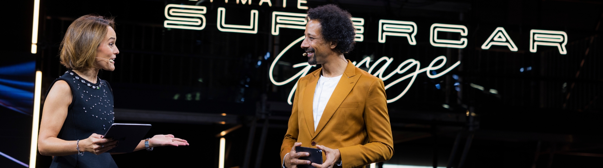 Black and white photograph of a journalist in a garage lit by neon lights, filming a supercar.