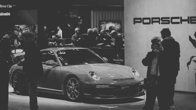 Photo noir et blanc d'une supercar Porsche sur un stand lors d'un salon, entouré par du public