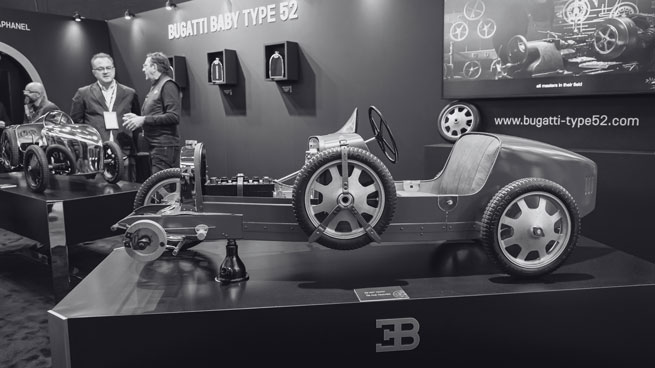 Photo noir & blanc d'un stand sur un salon de supercar présentant une véhicule sur un podium avec plusieurs personnes autour