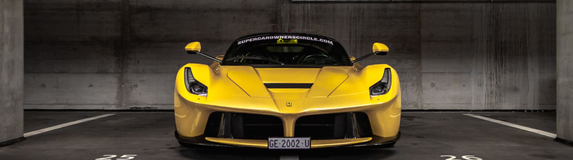 Yellow supercar parked in a parking lot against a dark background.